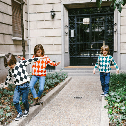 Niños haciendo equilibrio con jersey de rombos gris  naranja  y verde